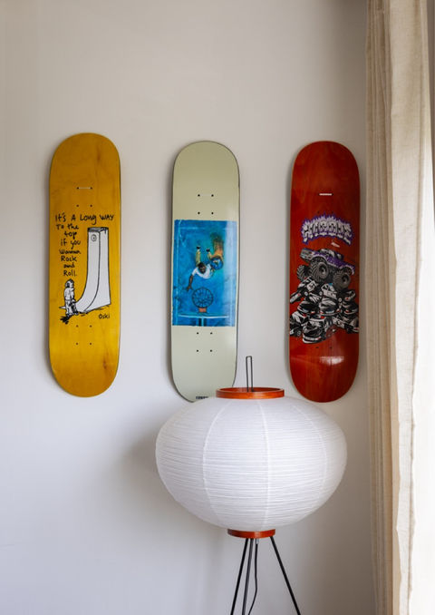 Three colorful skateboard decks mounted on a white wall above a round paper floor lamp with an orange accent in Hause House.