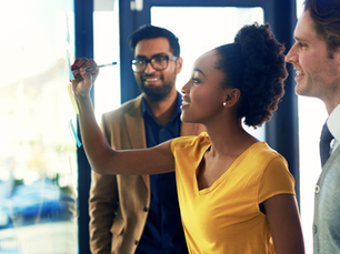 Three professionals smiling while a black female writes on a whiteboard.