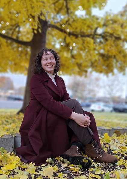 a photo of the author in a burgundy coat sitting in front of a yellow tree