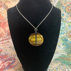A round tiger's eye stone wirewrapped to mimick an eye on a silver chain on a black necklace model form