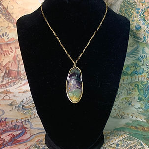 A wire wrapped fluorite stone with gold detailing on a silver chain on a black necklace model form