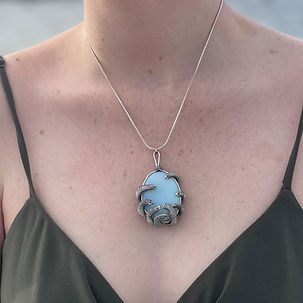 Closeup of an individual wearing a round opalite necklace wirewrapped in the style of an octopus holding the stone