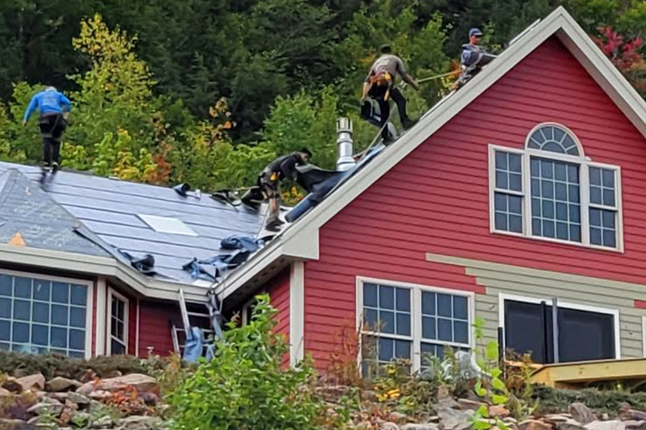 Roofers replacing shingles on red farmhouse