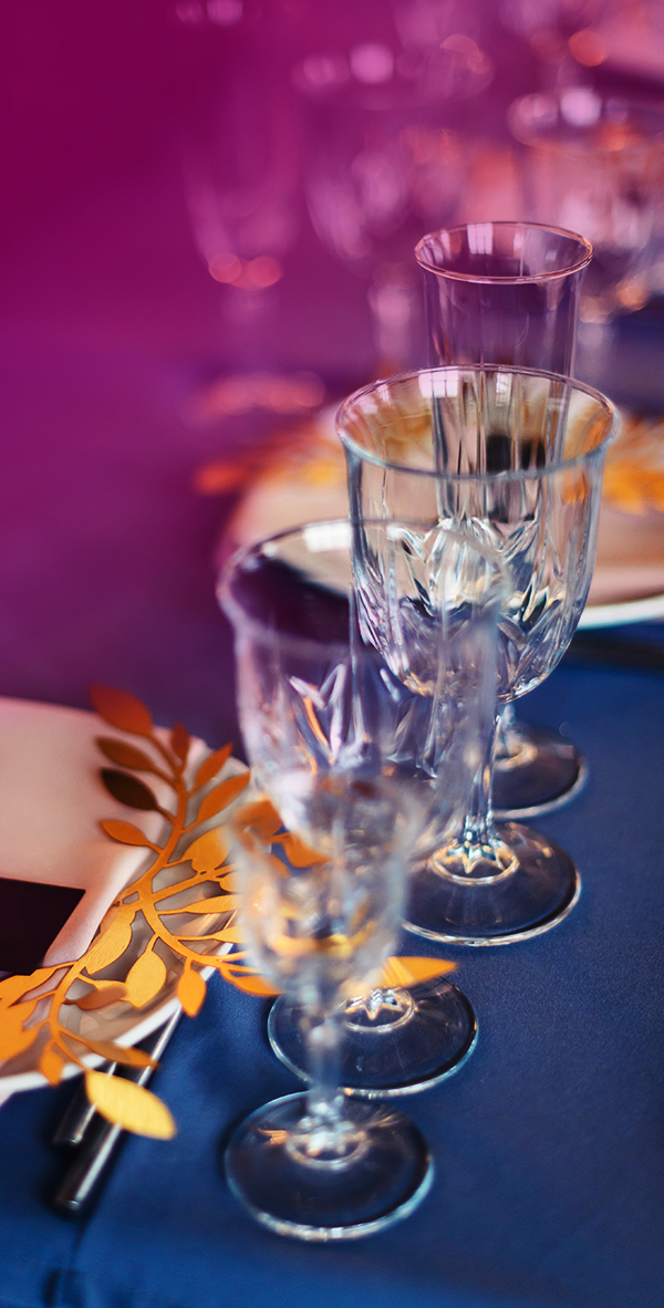Elegant crystal glasses set on a blue table with gold leaf place card