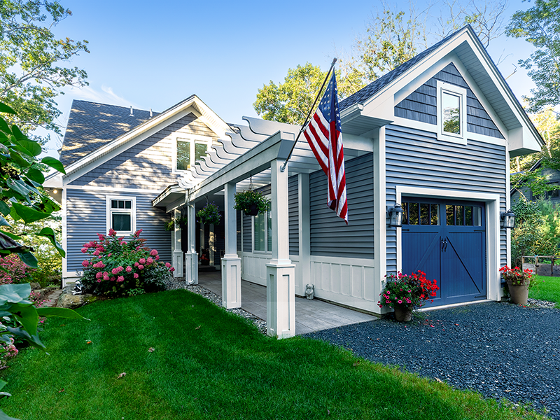 Beautiful gray house with American flag, spacious porch, and attached garage