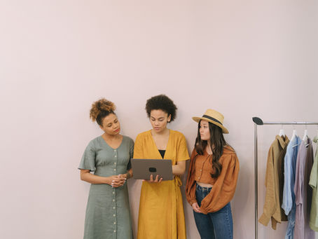 Three women discussing work beside clothing rails in a fashion boutique