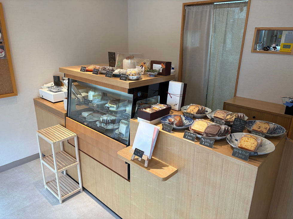 木目の棚にケーキやパウンドケーキ、パンが並ぶ店内の焼き菓子売り場。手書きの値札が見え、静かな雰囲気。