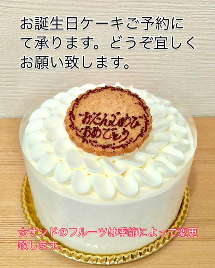 白いクリームの誕生日ケーキ。ケーキの上に「おたんじょうびおめでとう」とチョコで書いたクッキー。

画像内に予約案内の文字：
「お誕生日ケーキご予約にて承ります。どうぞ宜しくお願い致します」
「☆サンドのフルーツは季節によって変更いたします」