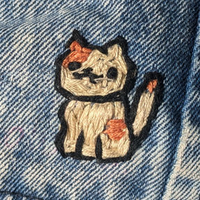An embroidered cat from the mobile game Neko Atsume: Kitty Collector on a pair of jeans