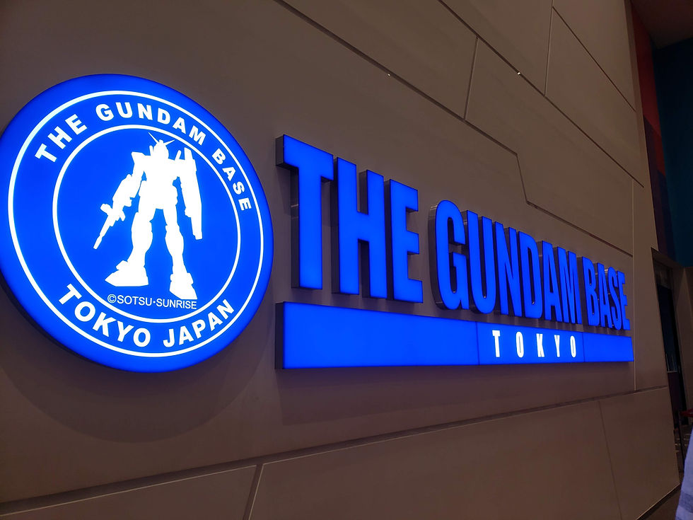 Blue illuminated sign of "The Gundam Base Tokyo" with a Gundam silhouette on a modern wall, conveying a high-tech, vibrant atmosphere.