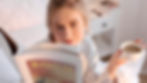 Women sitting on her bed reading a book and having a cup of tea.