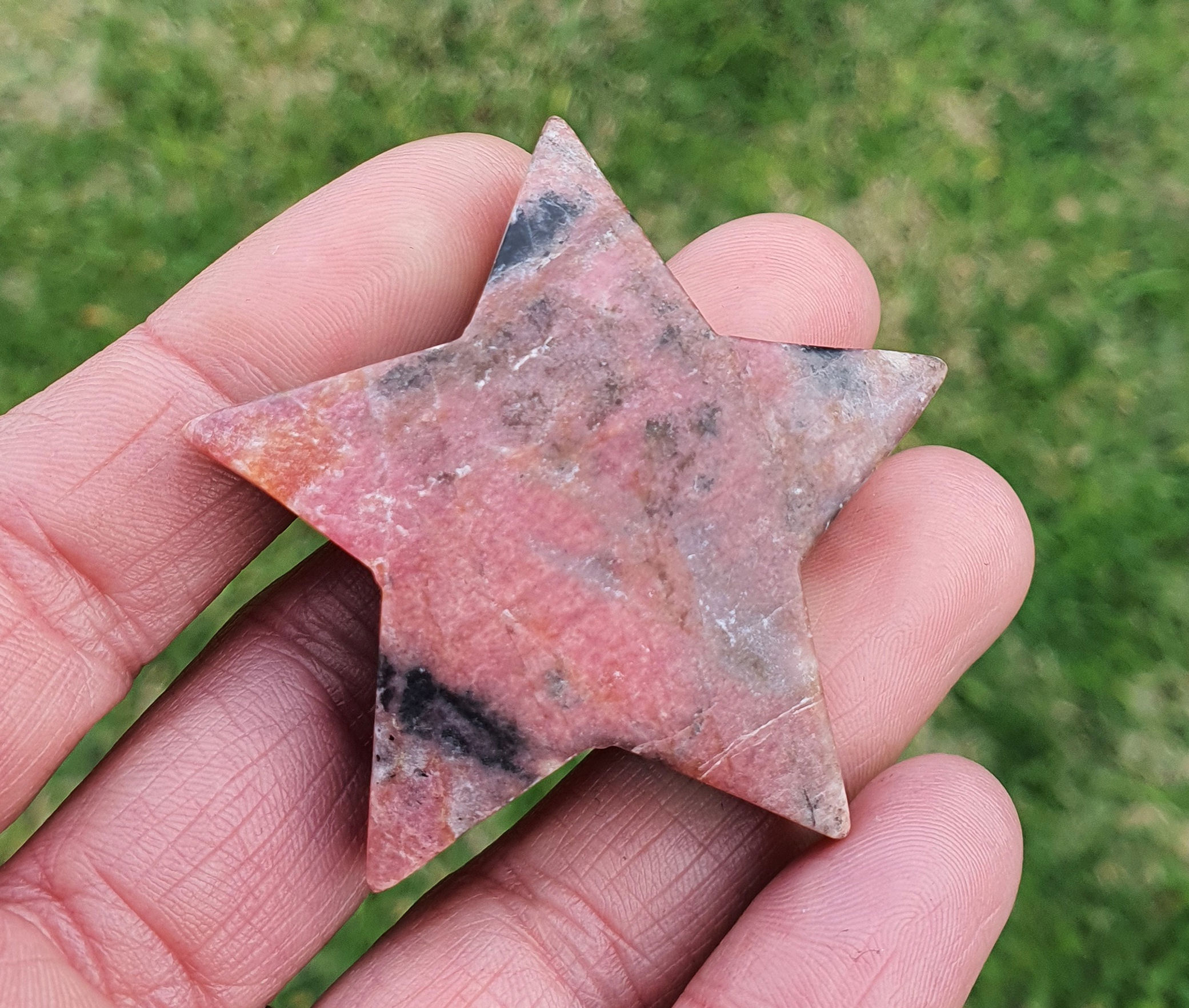 Hand holding a matte Rhodonite carved crystal star.