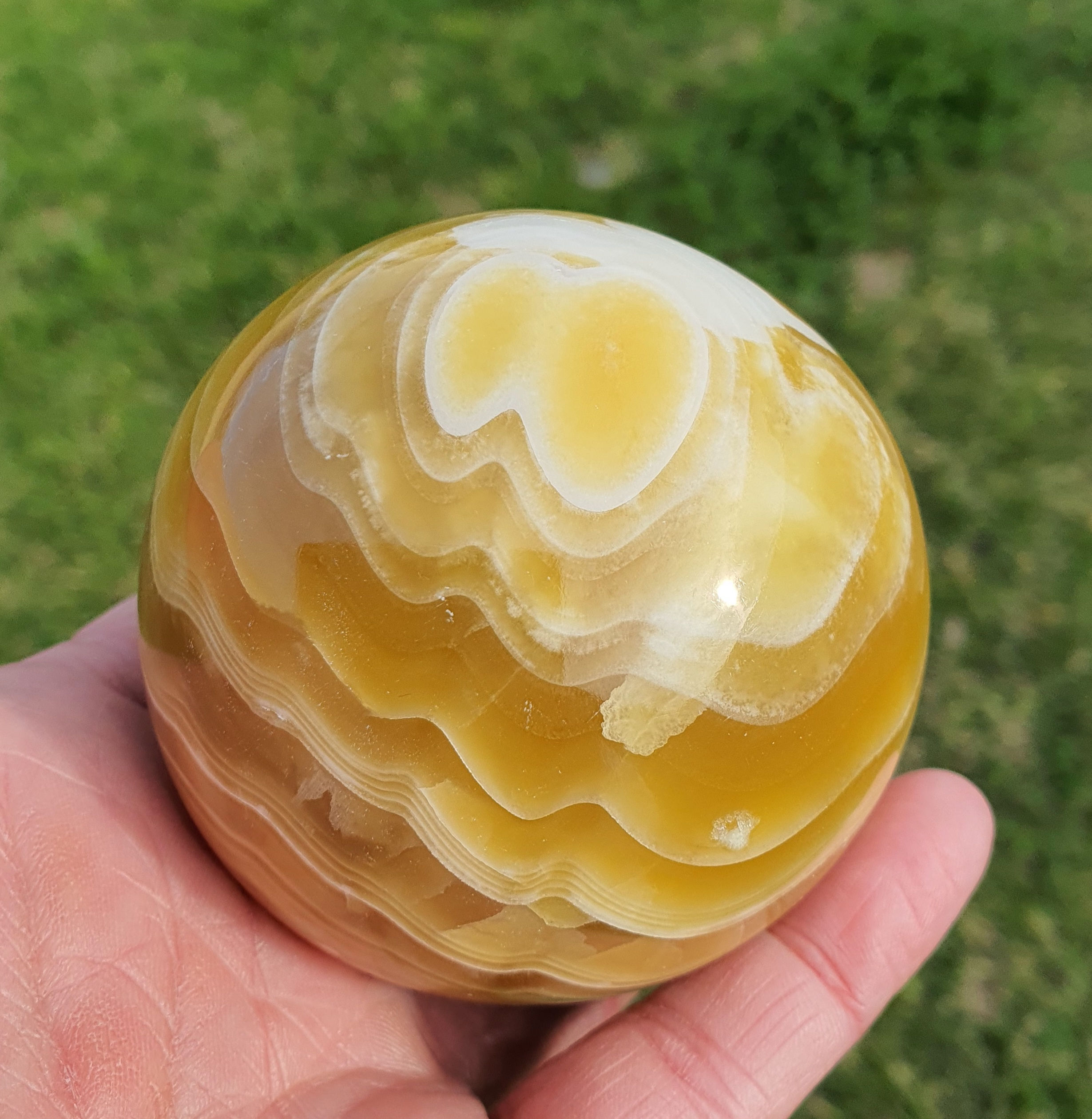 Banded honey calcite crystal sphere held in hand
