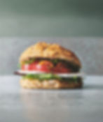 A homemade sandwich with goat cheese and lots of crispy vegetables on a smooth counter made out of mint green stone.