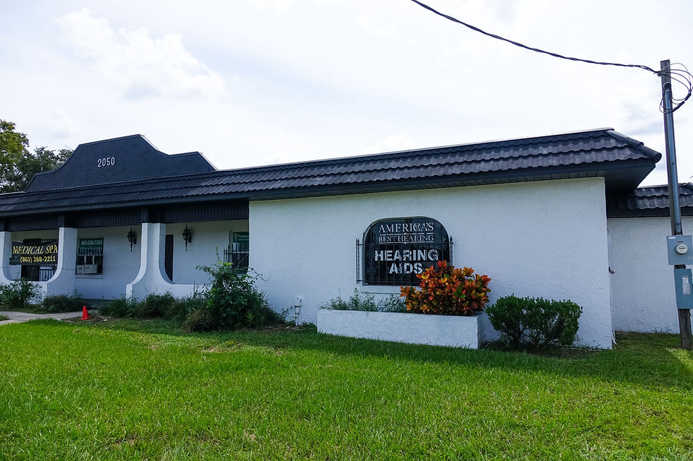 Exterior of a white building with a sign for Hearing Aids.