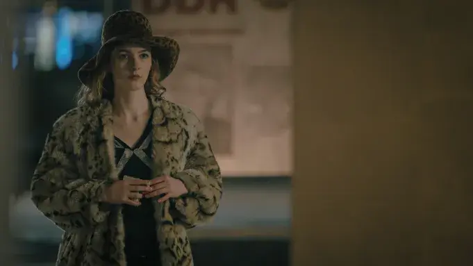 A woman in a leopard print coat and hat stands indoors, looking pensive. Background has soft lighting and blurred text. Mood is mysterious.