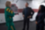 Three people are talking in a hallway. One wears a green tracksuit, the other two in suits. A wall logo shows 'FURY'. Serious mood.