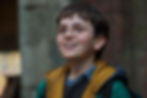 Smiling boy with round glasses, wearing a yellow and green jacket. Brick and stone background, conveying a sense of wonder and excitement.