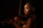 Woman with braided hair playing violin in dim light, wearing a sparkling dress. Focused expression, dark background.