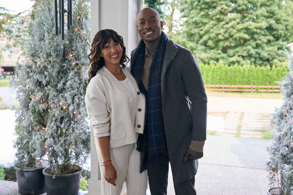 Smiling couple in winter clothing stands outside, surrounded by frosted trees with lights. A green hedge is visible in the background.