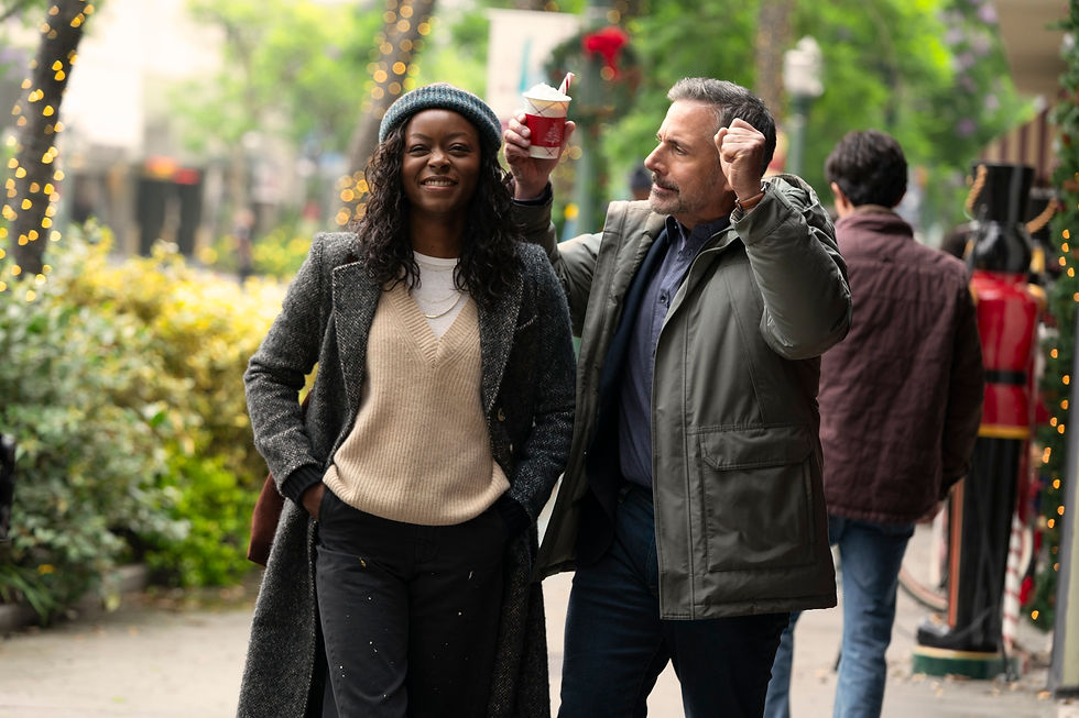 Man holds up a festive cup behind a smiling woman on a tree-lined street with holiday lights. Another person walks away. Cozy winter clothing.