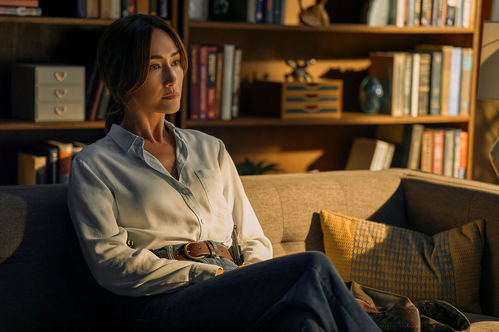 A woman in a white shirt sits on a couch, looking pensive. Background: bookshelves, decorative items. Warm lighting; cozy atmosphere.