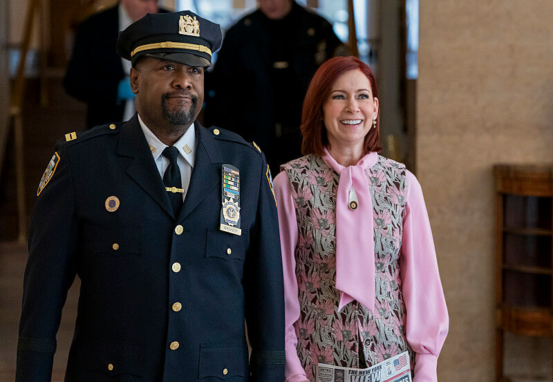 A police officer and a woman smile while walking indoors. The officer wears a uniform; the woman, a pink blouse with a patterned vest.