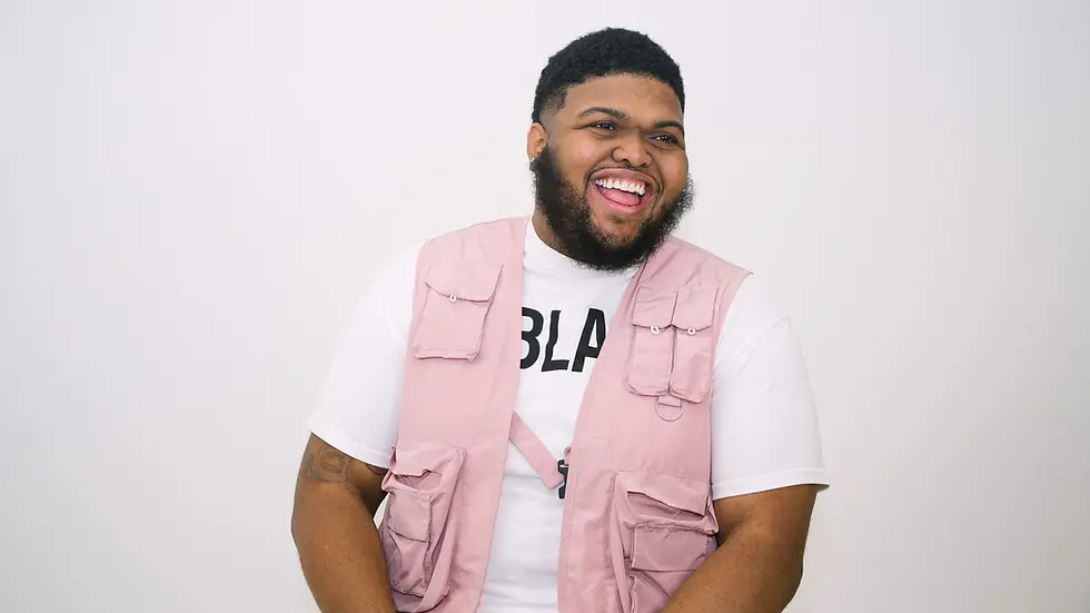 Smiling man in a pink vest and white T-shirt with BLA text, laughing against a plain white background.