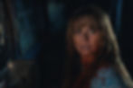 Bloodied woman with a frightened expression sits in a dark vehicle interior, looking over her shoulder.