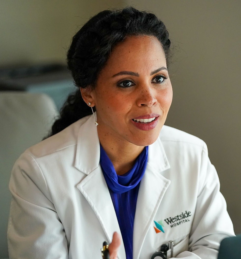 Woman doctor in a white Westside Hospital coat and blue blouse speaks in a calm office setting.