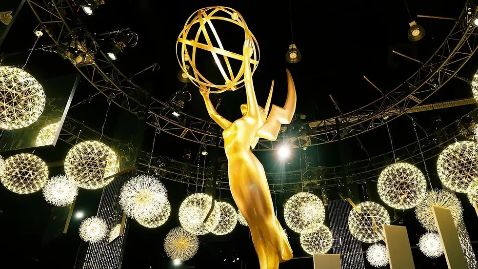 Golden Emmy statue stands amid glowing spherical lights, under a circular rig in a black background, creating a glamorous ambiance.