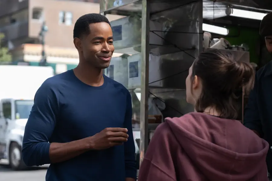 Man in blue shirt chatting with a woman at a street food cart, smiling on a city sidewalk.