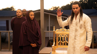 Three robed figures stand on a porch at dusk; a man in white raises his hand beside an ornate golden chair.