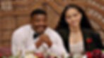 Smiling couple seated at a decorated table before a woven backdrop, with red flowers and an HD watermark.