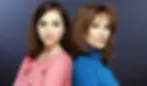 Two women standing back-to-back, one in a pink top with floral patterns, the other in a blue turtleneck, against a dark backdrop.