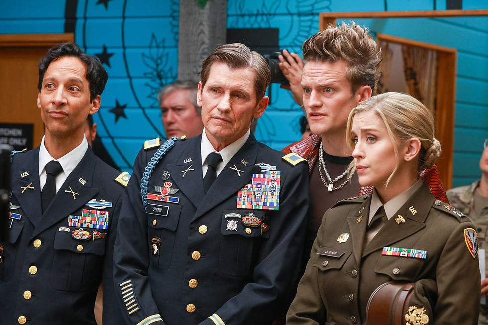 Four people in military uniforms stand together, looking focused. A blue wall with stars is in the background. Name tags read "Quinn."