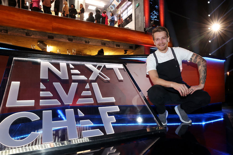 A chef in a white shirt and black apron kneels beside a lit "Next Level Chef" sign. People and a modern kitchen background are visible above.
