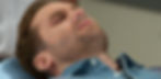 Close-up of a man lying in a hospital bed with a nasal oxygen tube, looking weak and pensive.