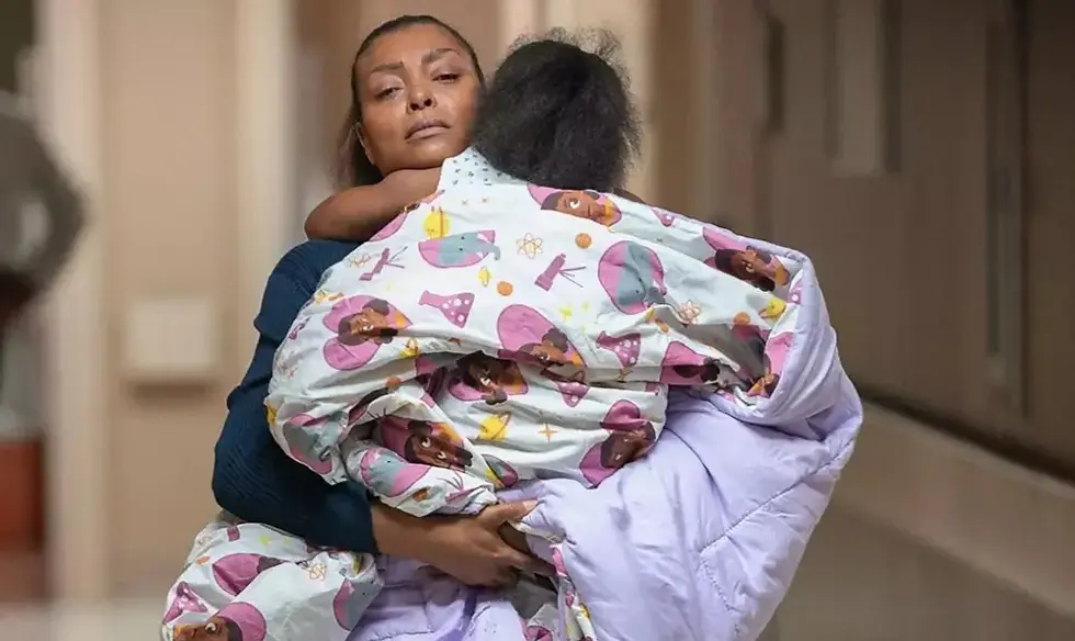Woman holds a child wrapped in colorful cartoon-patterned blankets. The hallway setting suggests a somber mood.