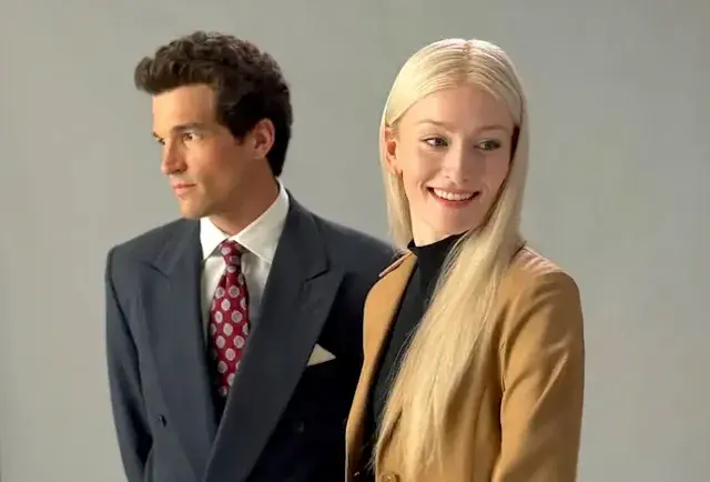 A man in a dark suit with a red tie looks left, while a woman in a tan jacket smiles right. Grey background, formal and cheerful mood.