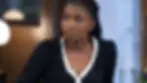 Concerned woman in a black dress with white trim looks off to the side in a softly lit indoor room.