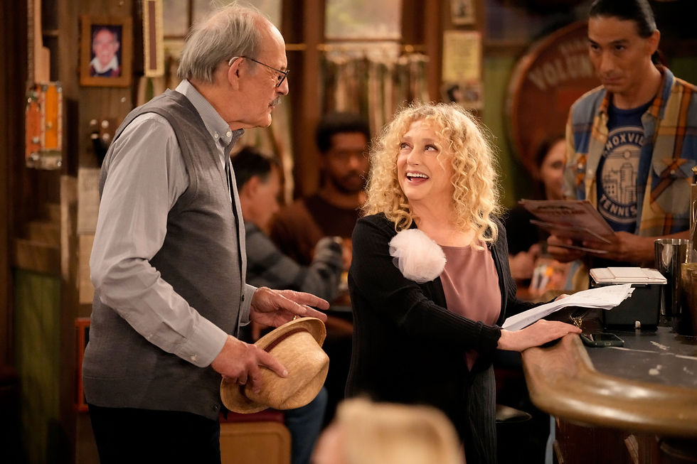 Elderly man holding hat talks to smiling woman at bar. Diverse patrons in casual setting. Warm lighting, decor suggests cozy atmosphere.