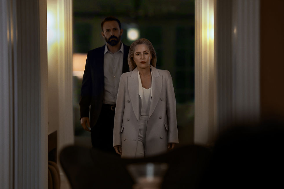 Serious woman in pale suit stands before bearded man in dark blazer in dim hallway, both facing forward under warm lights.