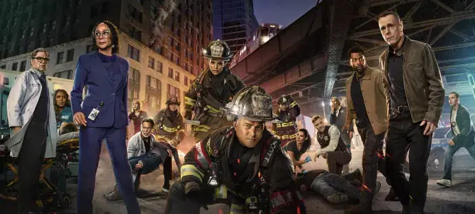 Firefighters and medical personnel work in an urban setting under a bridge at night, surrounded by high-rise buildings. The mood is intense.