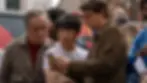 Three men closely examine a flyer in a busy urban setting. The mood appears curious and focused. Bright clothing adds a colorful touch.