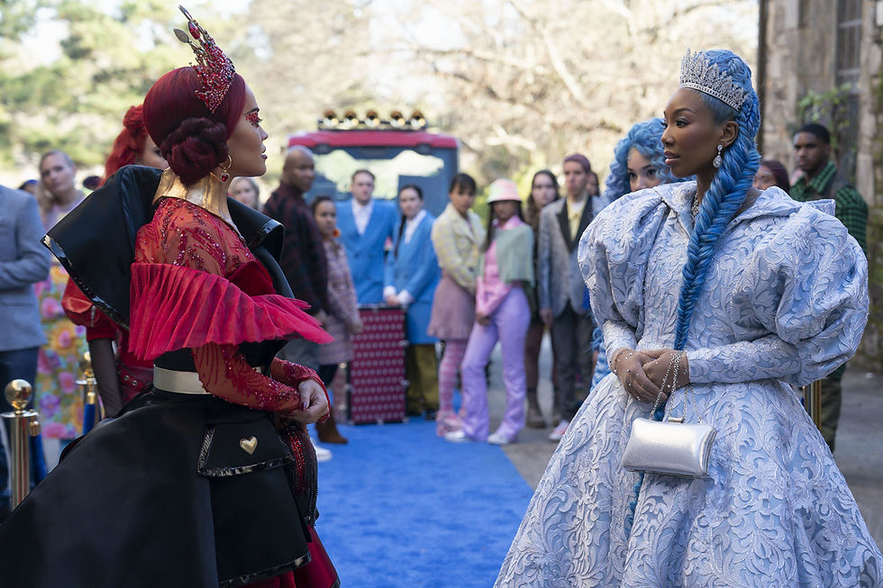 Two women in elaborate costumes face each other on a sunny day. One wears red with a crown, the other blue with a tiara. People watch nearby.