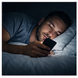Man looking at phone in bed in the dark