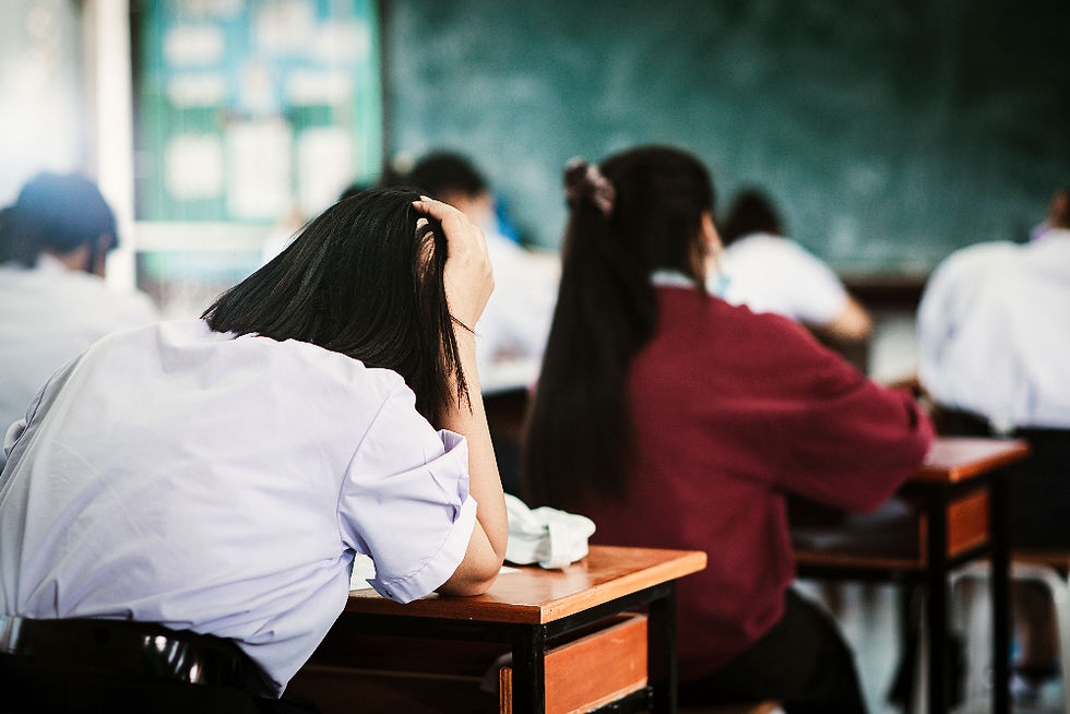 Élève en uniforme blanc, tête posée sur la main, dans une salle de classe; autres élèves flous devant un tableau vert, ambiance de classe