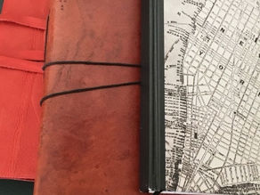 Carnet rouge en cuir avec élastique noir, couverture de carnet avec carte de New York, posés sur fond sombre.