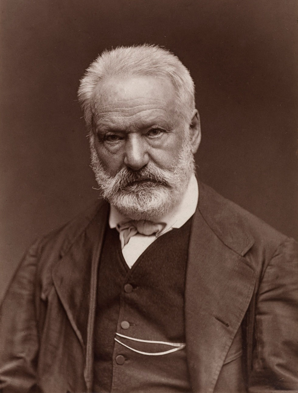 Portrait d’un homme âgé aux cheveux blancs et à la barbe blanche, en costume sombre, fond brun, regard sérieux.